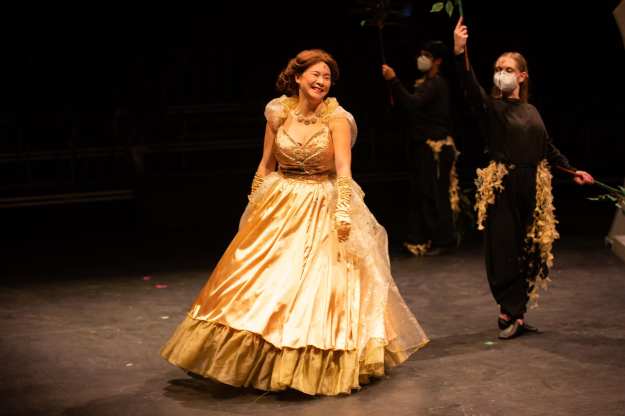 Actor in gold and silver ball gown, with dancer moving tiny birds around her